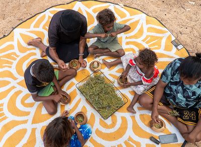 2 adults 4 children sitting cross legged in a circle on a round yellow mat