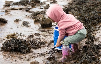 Child in pink hoody and boots raking sand and mud
