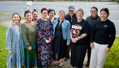 Group of 10 adults standing in front of water and grass and smiling